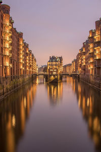 Illuminated buildings by river against sky at night