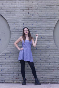 Full length portrait of young woman standing against brick wall