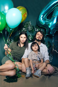 Family of three travelers sits on the floor of a studio against a green background