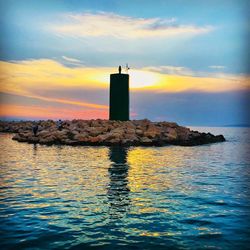 Lighthouse by sea against sky during sunset