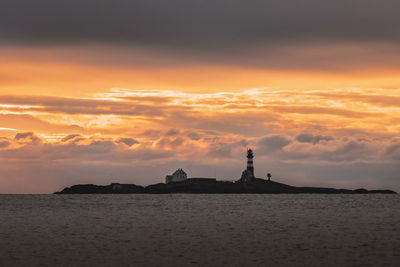 Silhouette of building by sea during sunset