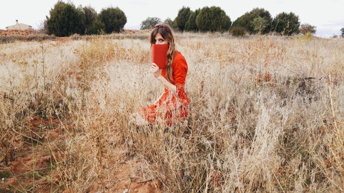 Portrait of mid adult woman with book kneeling on grassy field