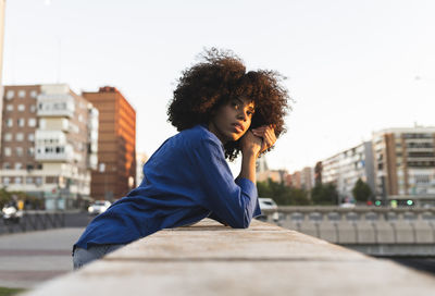 Thoughtful woman with afro hairstyle leaning on wall
