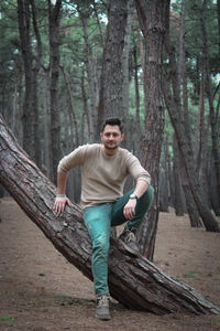 Portrait of man sitting on tree trunk at forest