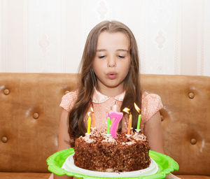 Cute girl blowing birthday candles on cake at home