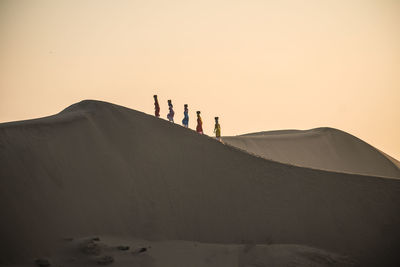 People standing on sand dune against clear sky