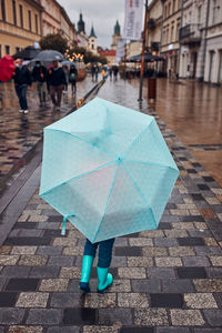 Back view of child holding big blue umbrella walking in a downtown on rainy gloomy autumn day