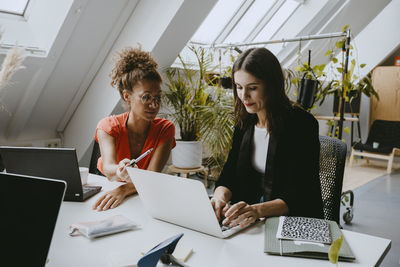 Female colleagues discussing over laptop at coworking office