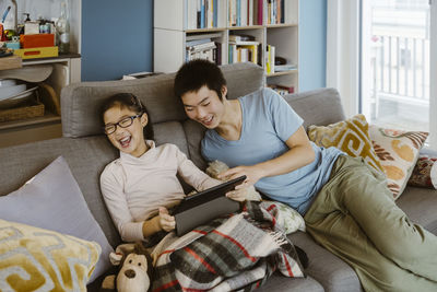 Happy siblings having fun watching digital tablet while reclining on sofa at home