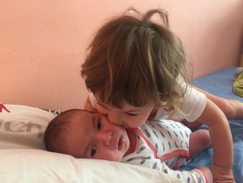 Sister kissing baby brother on bed
