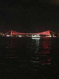 Illuminated bridge over river against sky at night