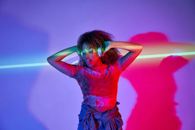 Woman with arms raised standing against pink background