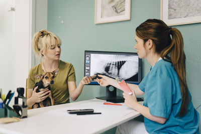 Female veterinarian giving medicine to woman with terrier dog in medical clinic