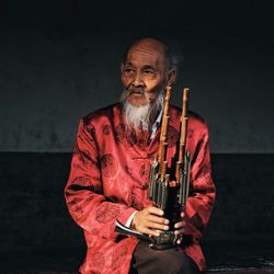 Senior man holding musical instrument while sitting against wall