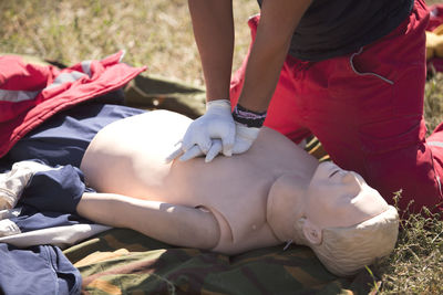 Low section of man practicing cpr on dummy at field during sunny day