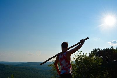 Rear view of man holding bamboo against sky