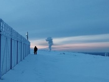 Rear view of person walking on snow covered field against sky