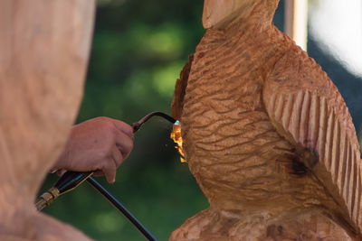 Cropped image of man using blow torch on wooden sculpture