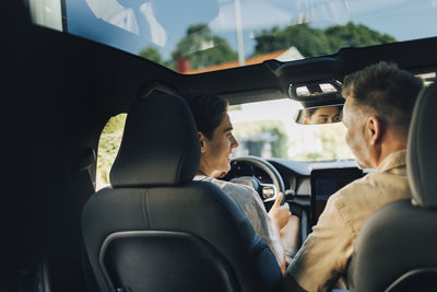 Rear view of father assisting son in driving car