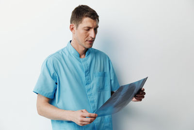 Portrait of young man using mobile phone while standing against white background