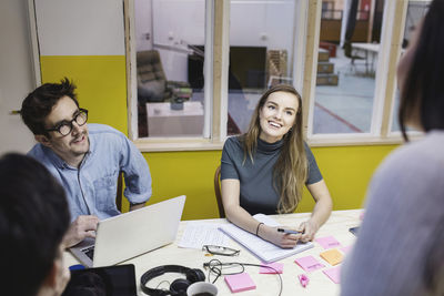 Happy young woman looking at colleague during meeting in creative office