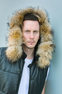 Portrait of man wearing fur hood against blue wall