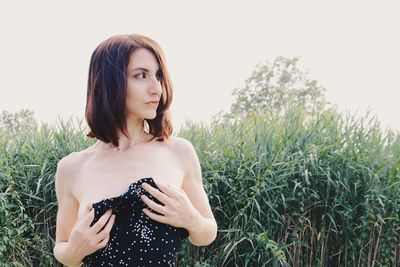 Beautiful young woman standing on field against sky