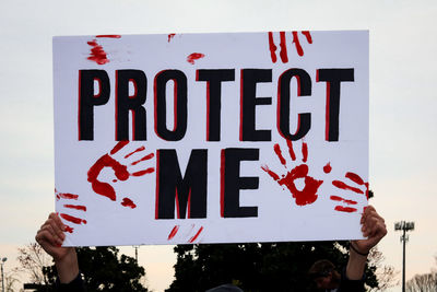 Close-up of hand holding text against the sky