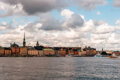 View of buildings by river against cloudy sky