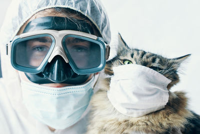 Portrait of man with cat wearing mask against white background