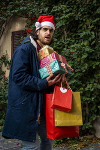 Young man with santa claus hat has a surprised expression and brings his newly purchased gifts.