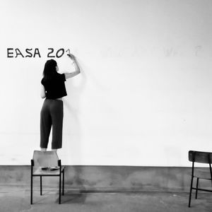 Rear view of woman standing on bench against wall