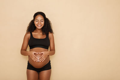 Smiling pregnant woman against beige background