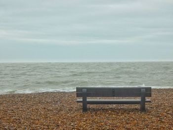 Empty bench on shore by sea against sky