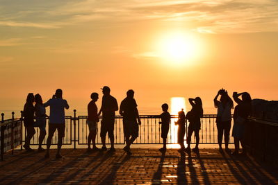 Silhouette of people standing by railing against sky during sunset