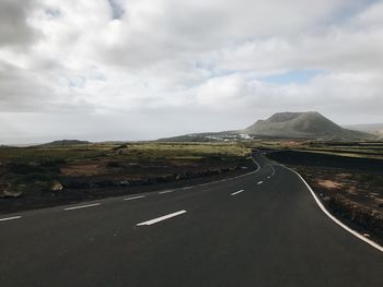 View of road along landscape against cloudy sky