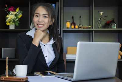 Portrait of smiling woman using phone while sitting on table