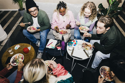 High angle view of multiracial male and female students enjoying food in college dorm