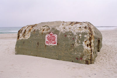 Information sign on rock by sea against clear sky