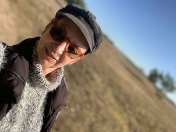 Close-up portrait of woman wearing sunglasses standing on field against clear sky during sunny day