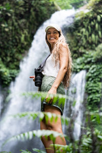 Portrait of smiling young woman standing against trees