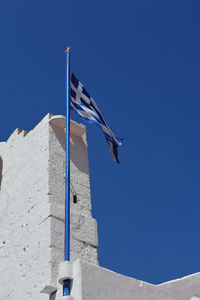 Low angle view of flag against building against clear blue sky