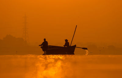 Silhouette people in boat on sea against orange sky