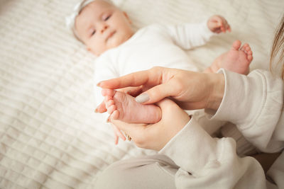 Mother massages her little daughter, newborn baby. lies on bed in bedroom, homely. legs, fingers. 