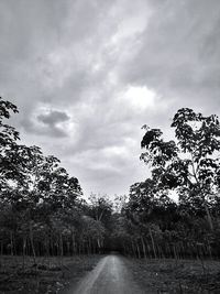 Road passing through field against cloudy sky