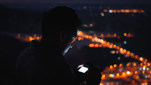 Side view of woman holding illuminated string lights at night