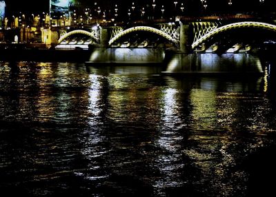 Illuminated bridge over river in city at night