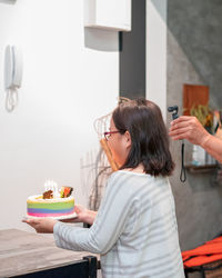 Girl holding cake while standing against wall