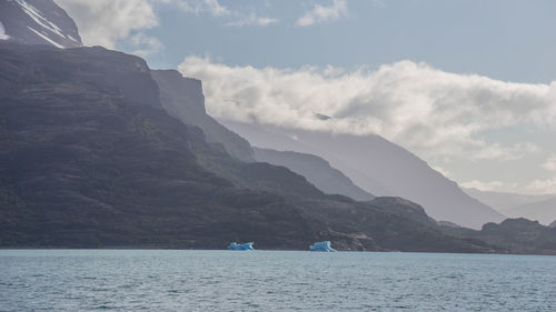 Scenic view of sea by mountains against sky