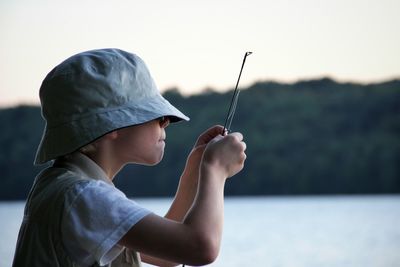 Side view of boy holding stick against lake